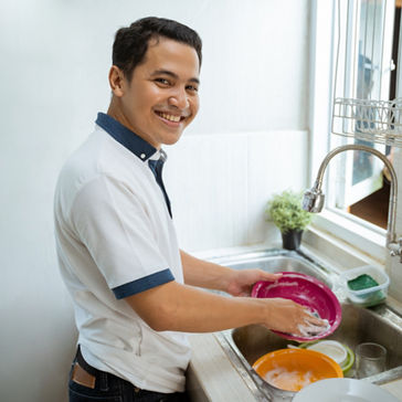Jóvenes asiáticos felices con camisa blanca parados y lavando los platos en la cocina