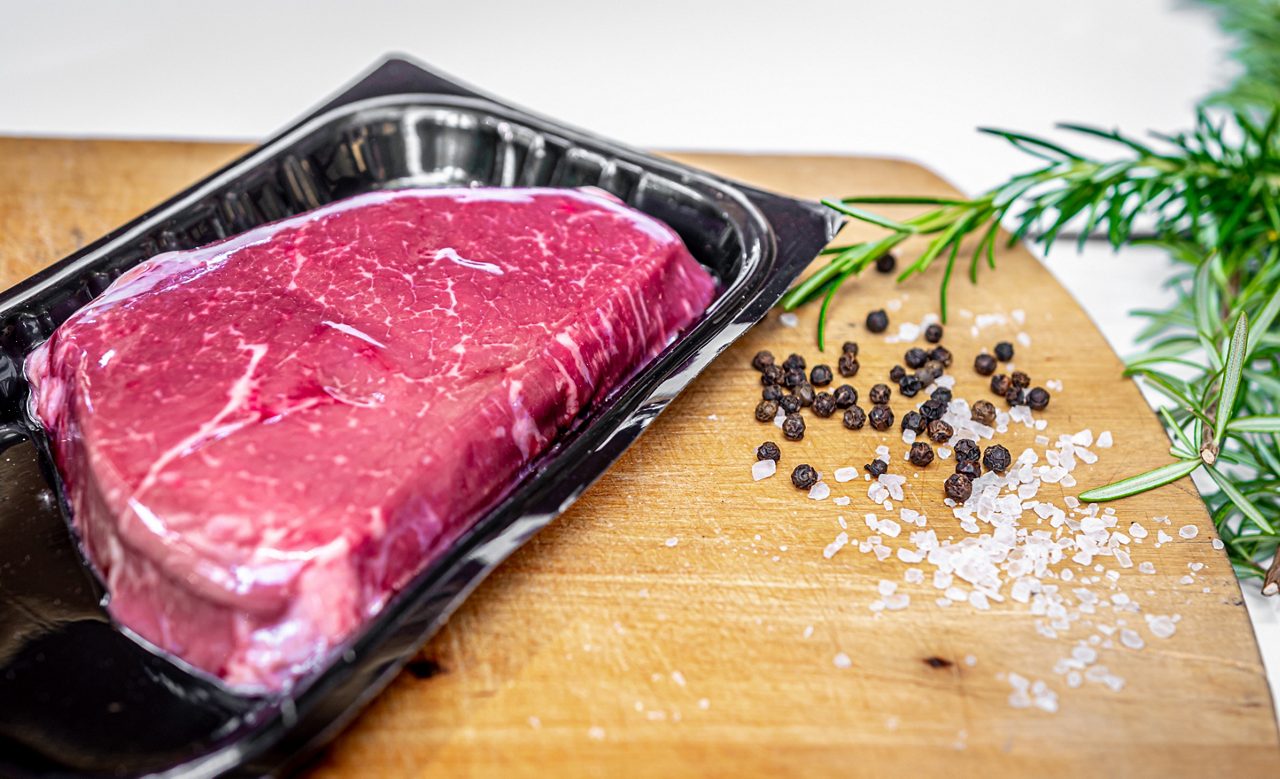 Raw beef steak in vacuum skin packaging and spices on wooden chopping board