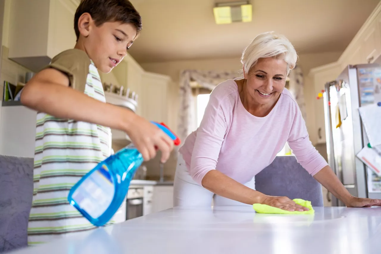 Grandmother and grandson cleaning the kitchen table with cloth and cleaning spray