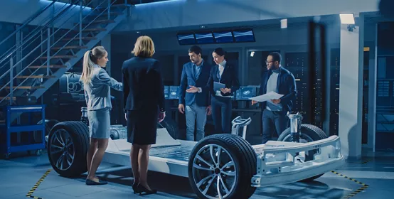 Diverse Team of Automobile Design Engineers Introducing Futuristic Autonomous Electric Car Platform Chassis to a Group of Investors and Businesspeople. Vehicle Frame with Wheels, Engine and Battery