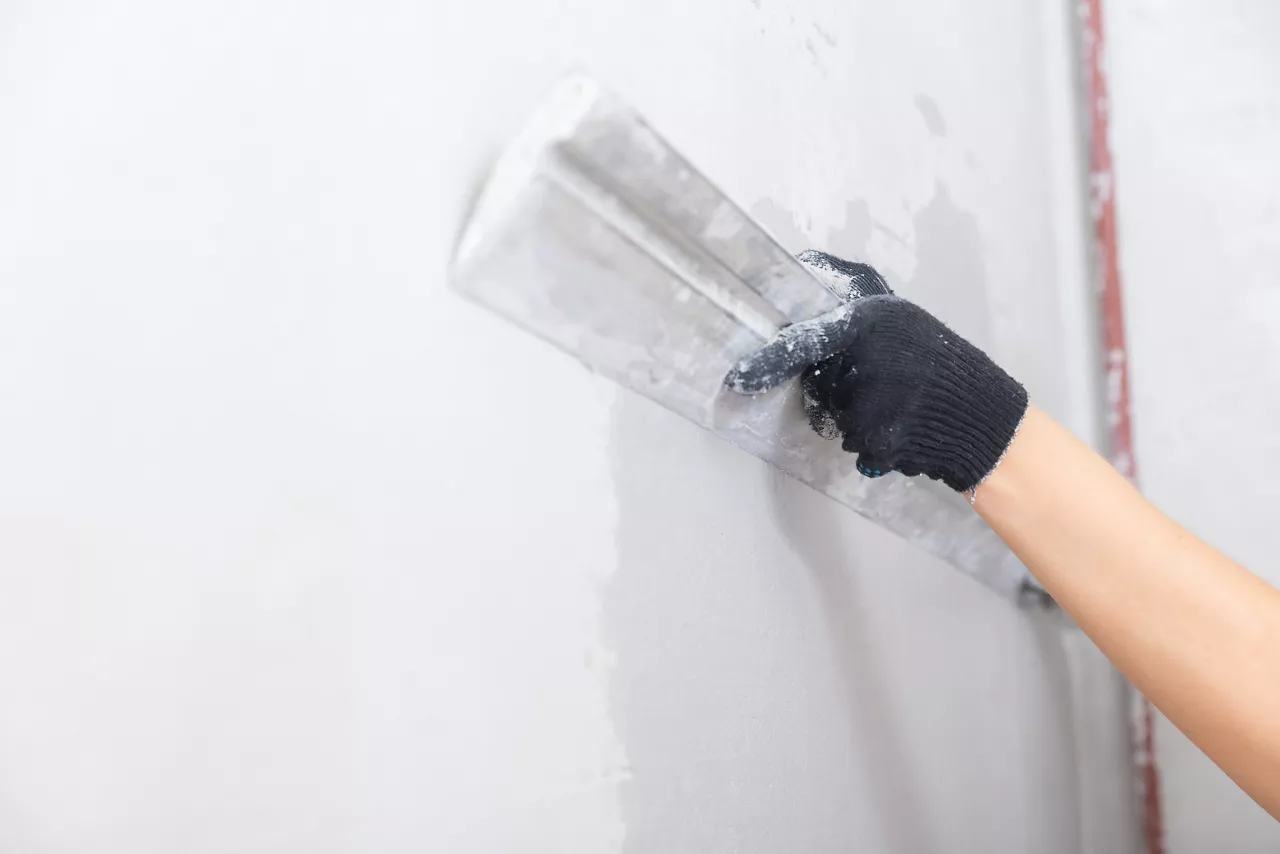 Construction worker applies plaster with trowel to concrete