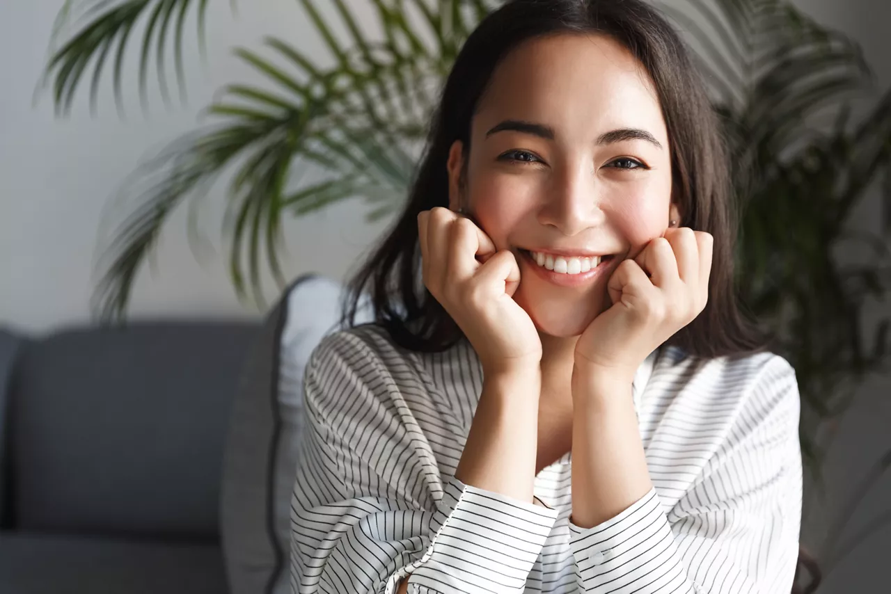 Portrait of attractive smiling asian woman looking happy at camera, resting at home. Female korean girl relaxing, have lazy weekend inside, like new apartment.