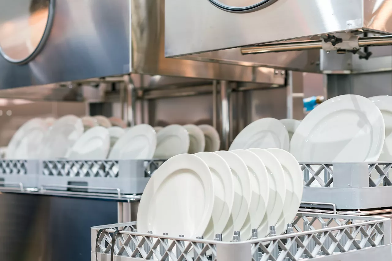 White plates arranged on basket for cleaning by automatic dishwasher machine in kitchen restaurant 