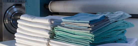 Stack of folded clean sheets or fabrics and industrial iron in an industrial laundry. Cleaning and ironing service for hotels, hospitals, clinics and companies.