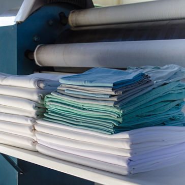 Freshly laundered and folded bright white, green and blue linens in institutional laundry facility 