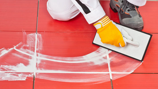 Grout being spread on red floor tiles