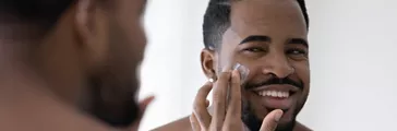 Man applying natural  moisturizer to his face in the mirror