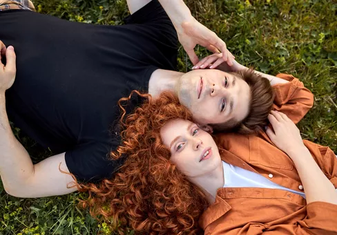 Top view on beautiful couple lying on grass in field at summer day, enjoying nature