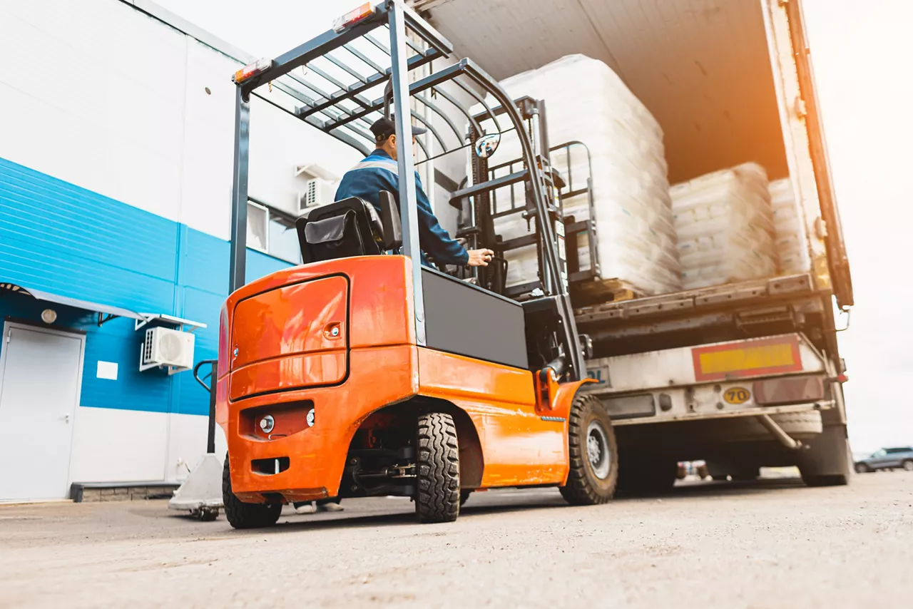 A man on a forklift works in a large warehouse, unloads bags of raw materials.