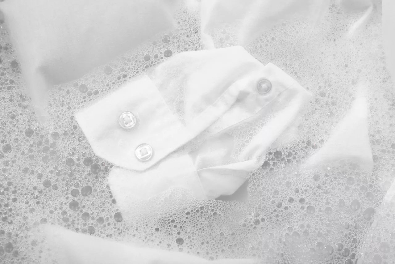 White button-down shirt sleeve soaking in soapy water