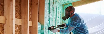Worker spraying polyurethane foam for insulating wooden frame house.