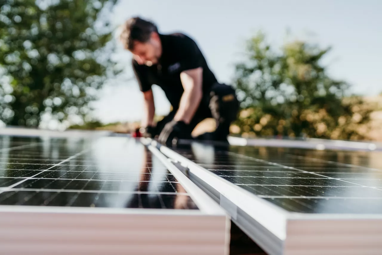 Mature Technician man assembling solar panels on house roof for self-consumption energy. Renewable energies and green energy concept. focus on foreground.