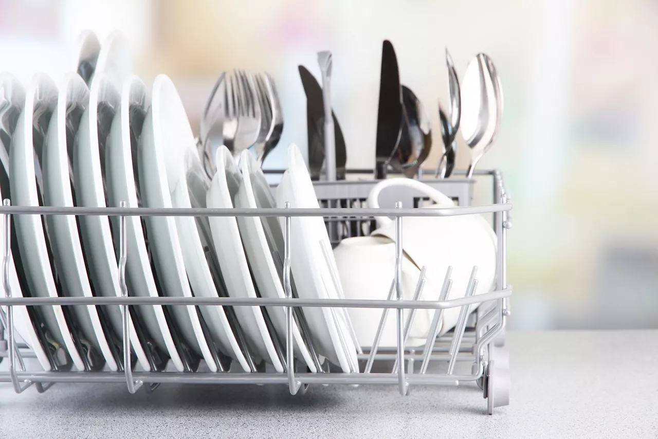 Dishrack with drying dishes and forks, spoons and cutlery.