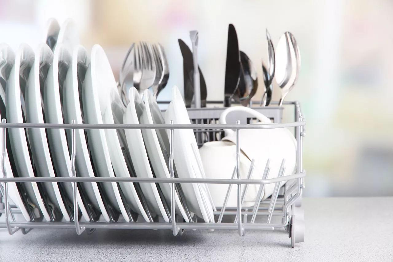 Clean dishes drying on metal dish rack on light background