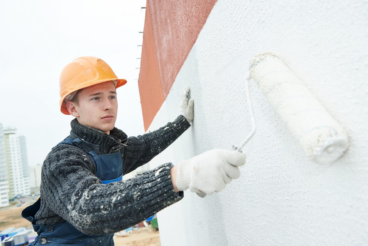 Builder worker painting facade of high-rise building with roller.