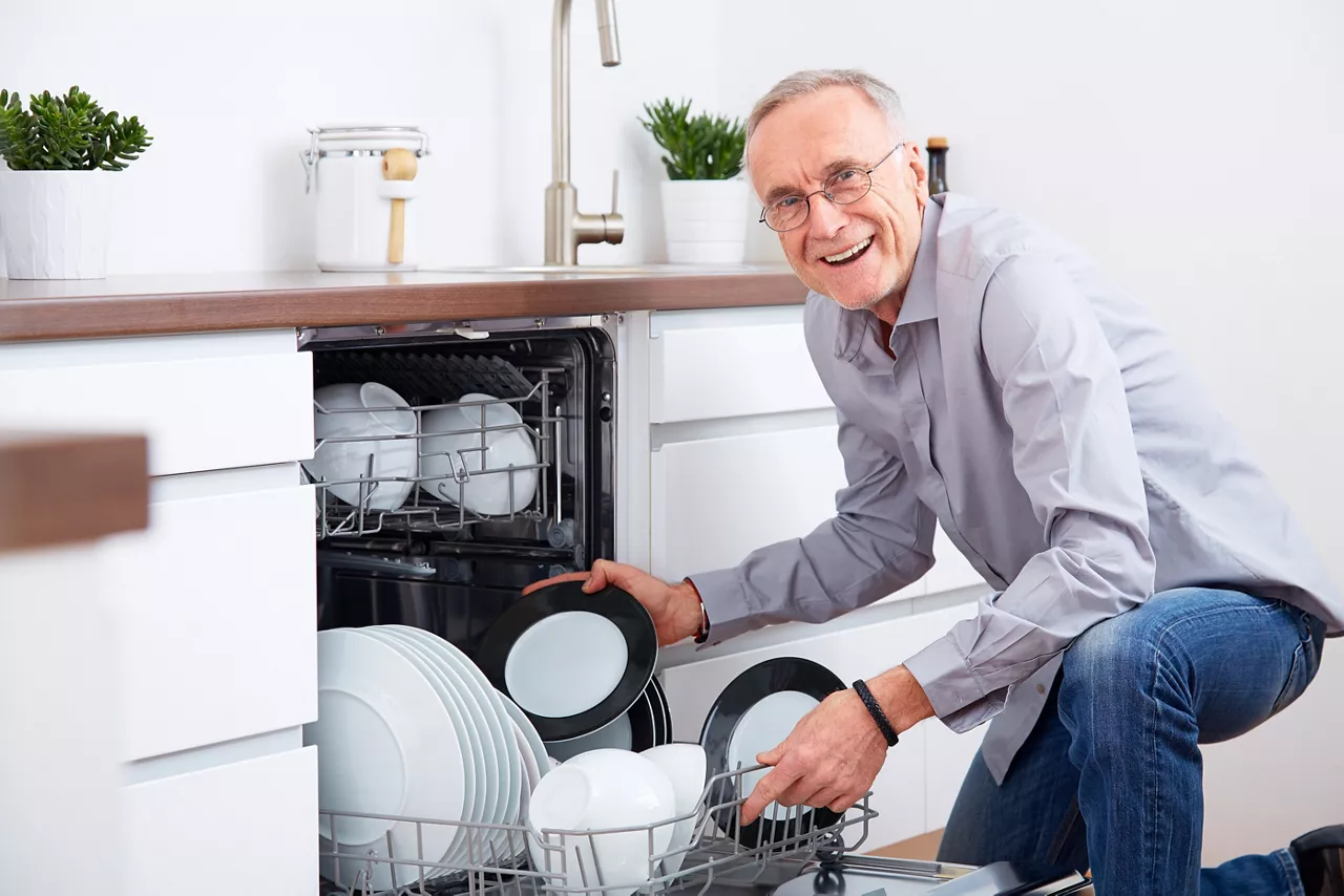 Older man taking dishes out of dishwasher