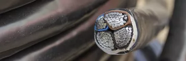 Cross section of electric black industrial underground cable on large wooden reel. Four core al cable. Selective focus and shallow dof.