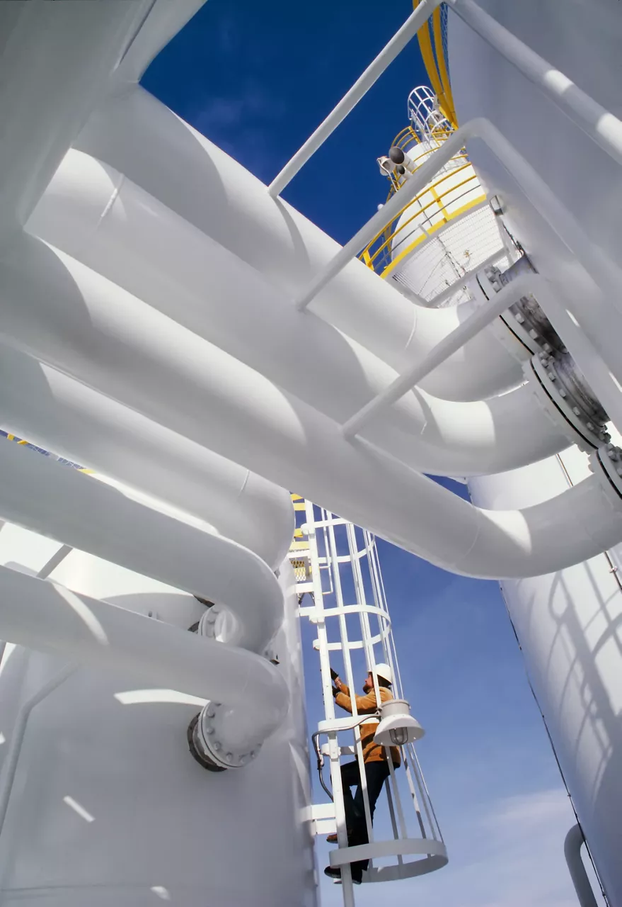 Industrial worker at an oil and gas processing plant climbing a ladder