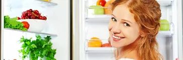 Happy woman standing at the open refrigerator with fruits, vegetables and healthy food