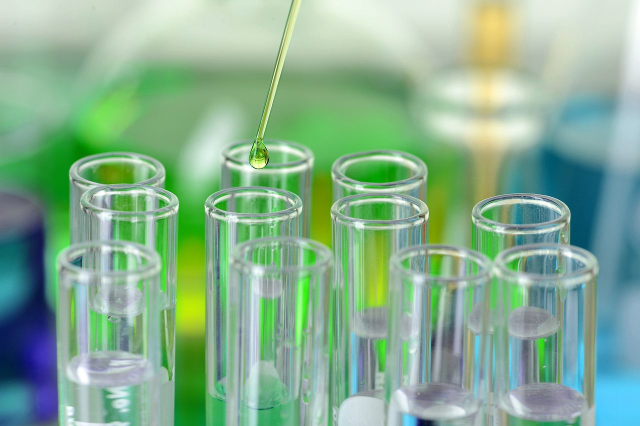 Green liquid dripping from pipette into laboratory test tubes