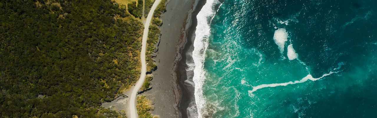 Drone point of view of a single lane road passing next to a coast.