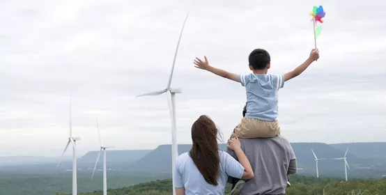 Little boy sitting on dads shoulders, with mom next to them overlooking windmills. 