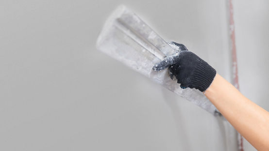 Worker applying drywall cladding on wall using scraper. 