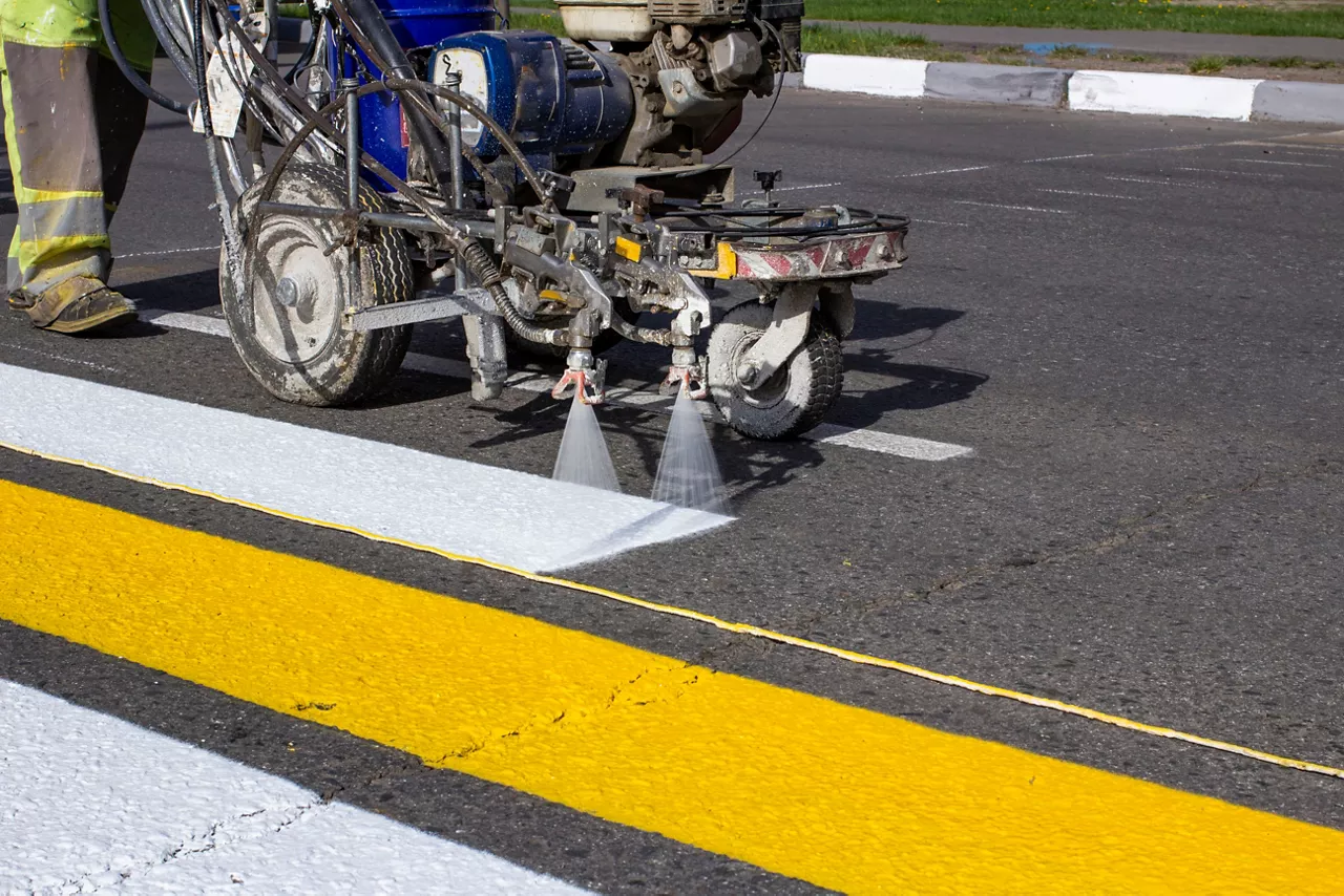 Road workers use hot melt scribing machines to paint pedestrian crosswalk on asphalt road surface 