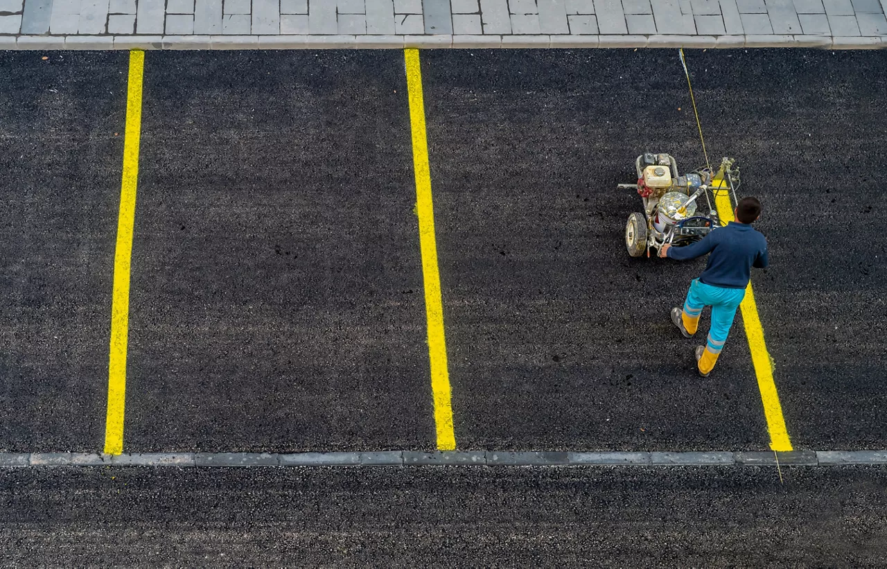 Worker paints a yellow line on an asphalt parking lot  