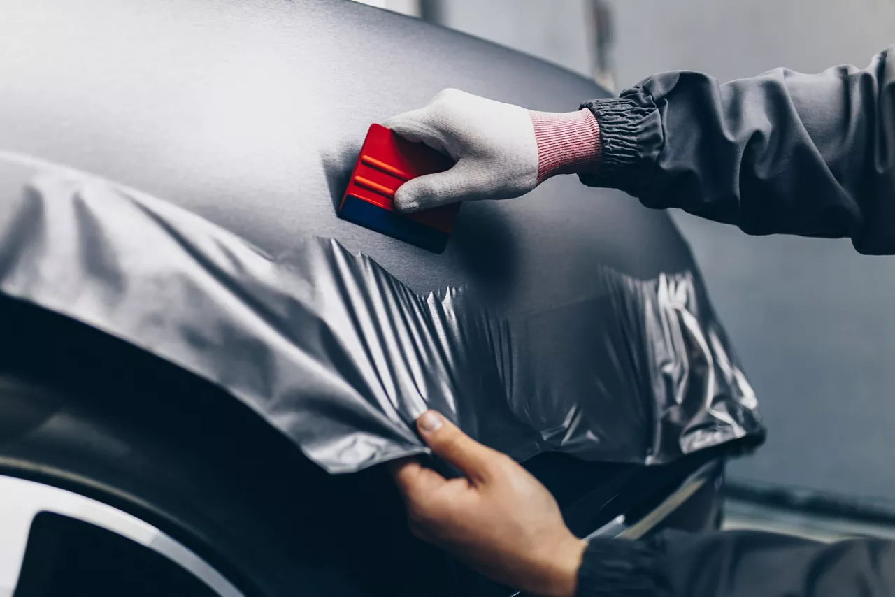 Car wrapping specialist putting vinyl foil or film on car. Selective focus.