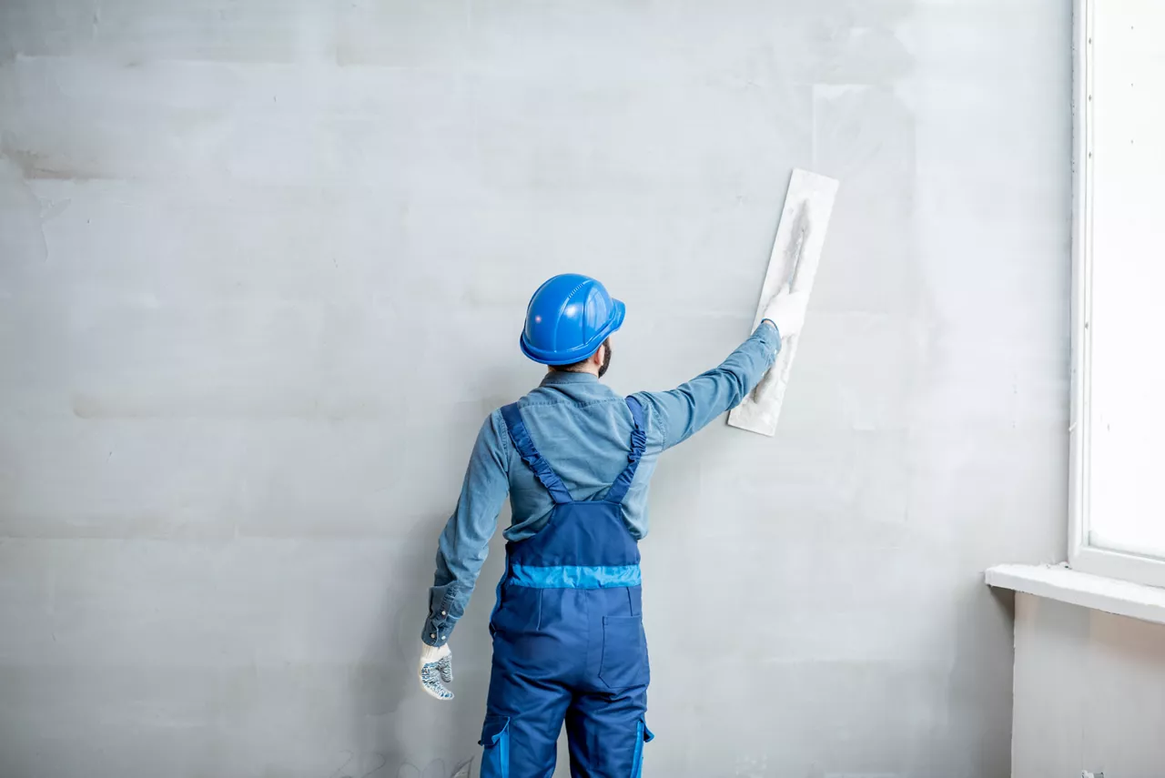 Plasterer in blue working uniform plastering the wall indoors