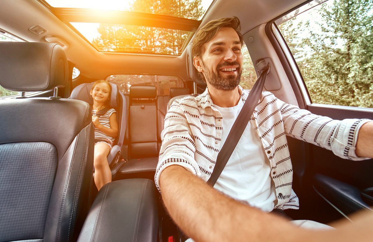 Familia conduciendo un automóvil, padres mirando a su hija en el asiento trasero