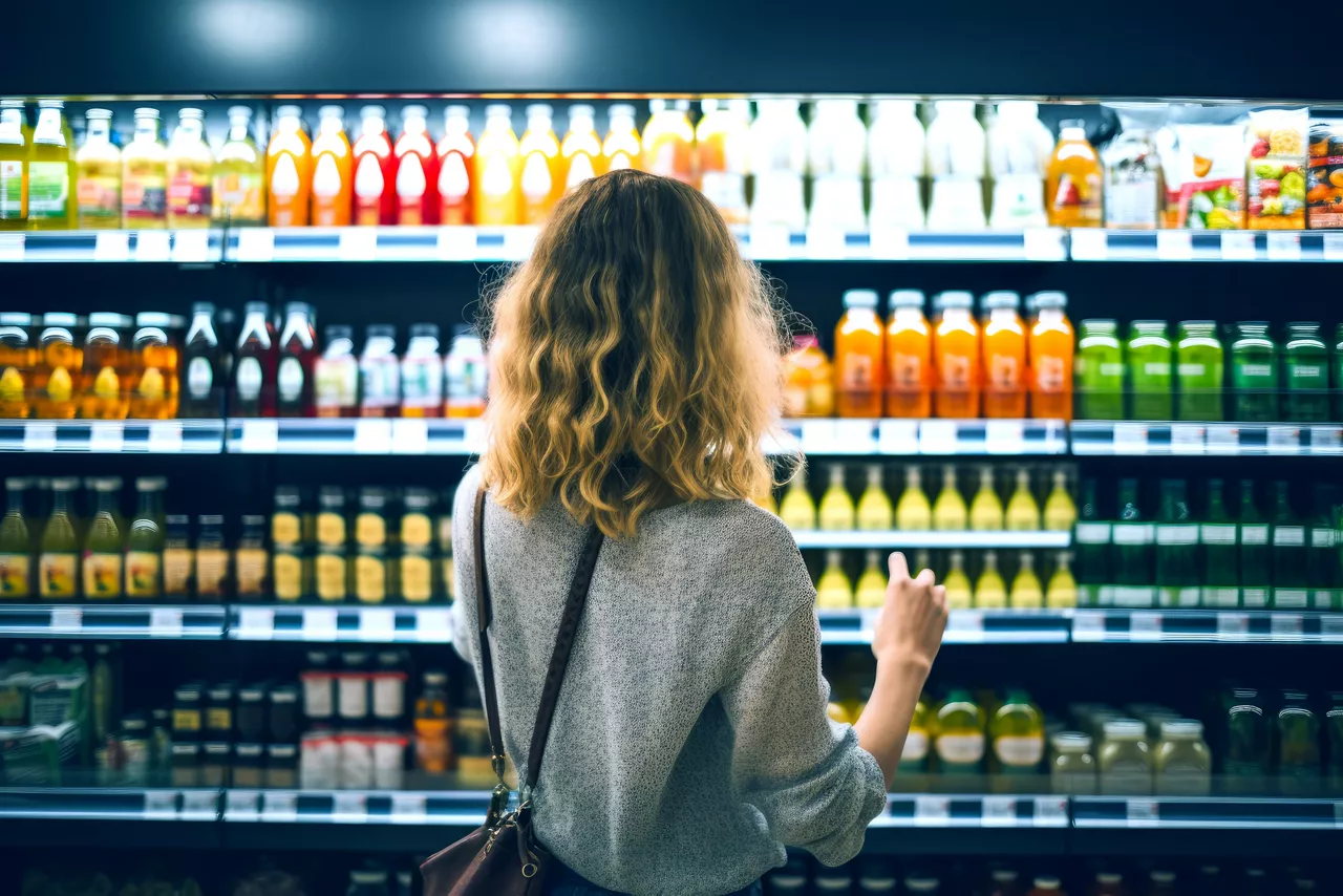 back view of young woman looking at bottle of juice in grocery store | K2025 color edit