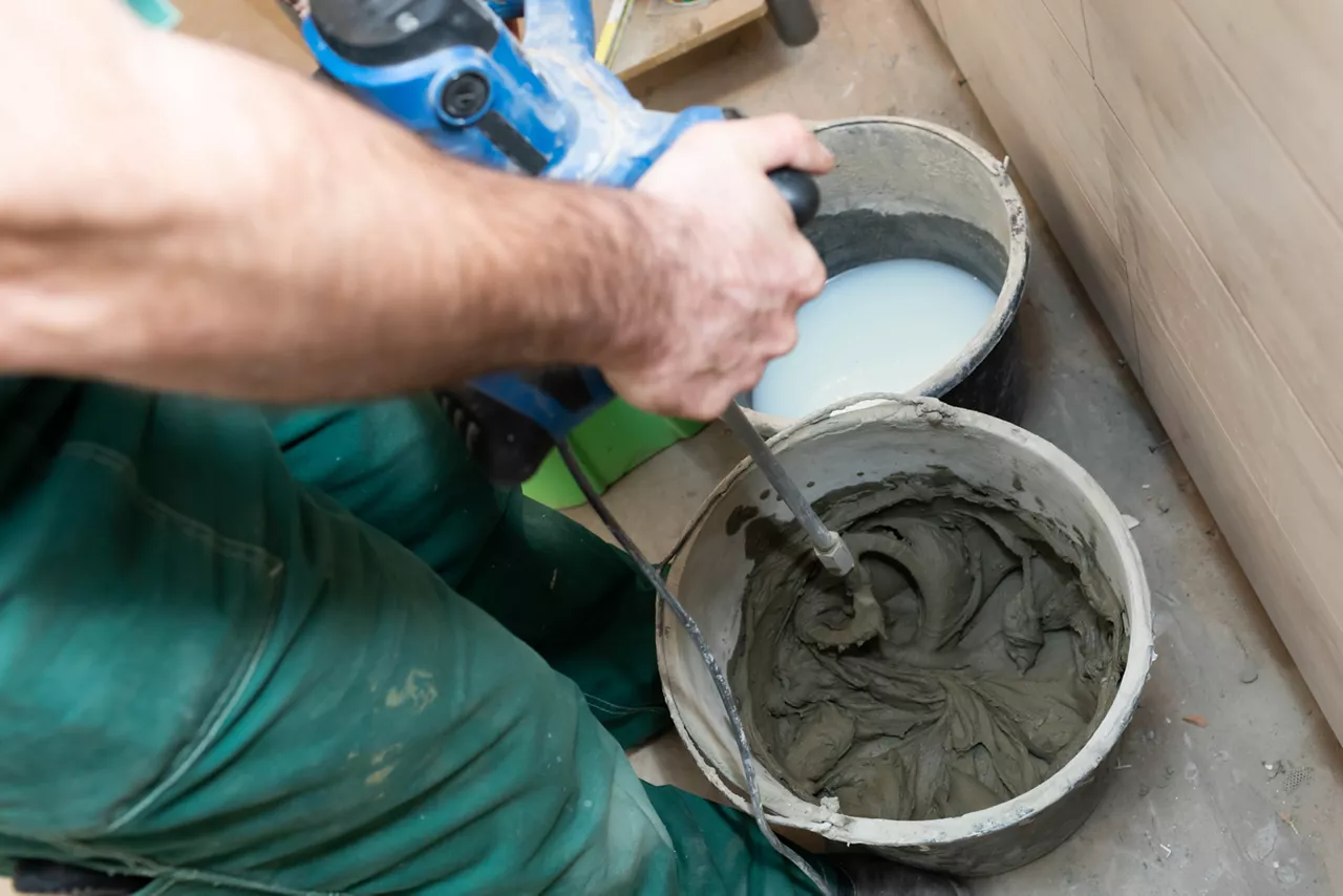 Worker mixing cement in a bucket using a power tool. 