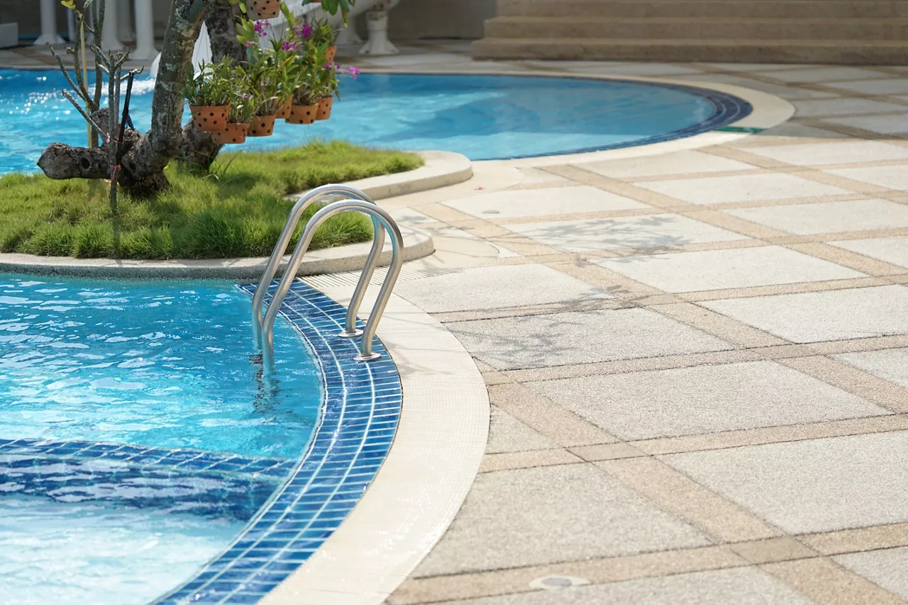 Outdoor pool with tiled surface and ladder.