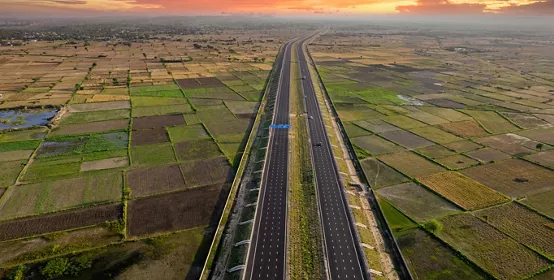orbit aerial drone shot of new delhi mumbai jaipur express elevated highway showing six lane road with green feilds with rectangular farms on the sides