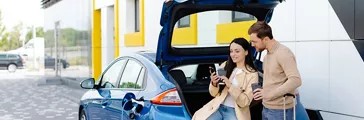  Friends charging automobile battery from public station and standing near electric car. 