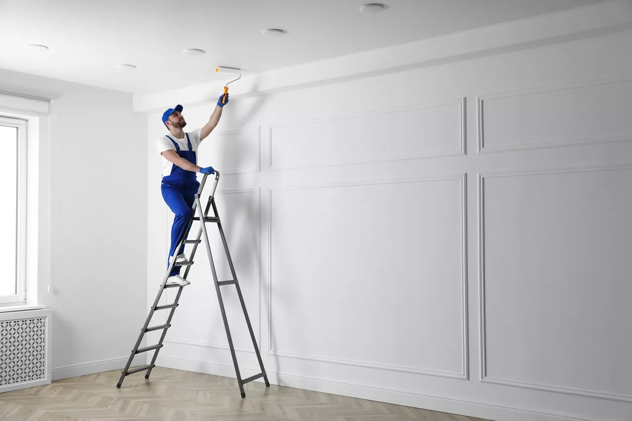 Handyman painting ceiling with white dye indoors, space for text