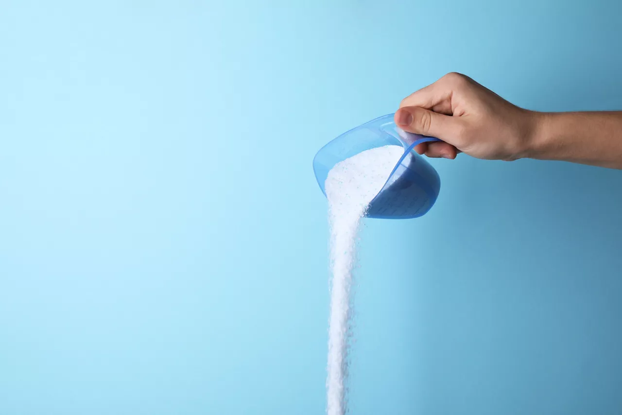 Woman pouring laundry detergent from measuring container against blue background, closeup. Space for text  