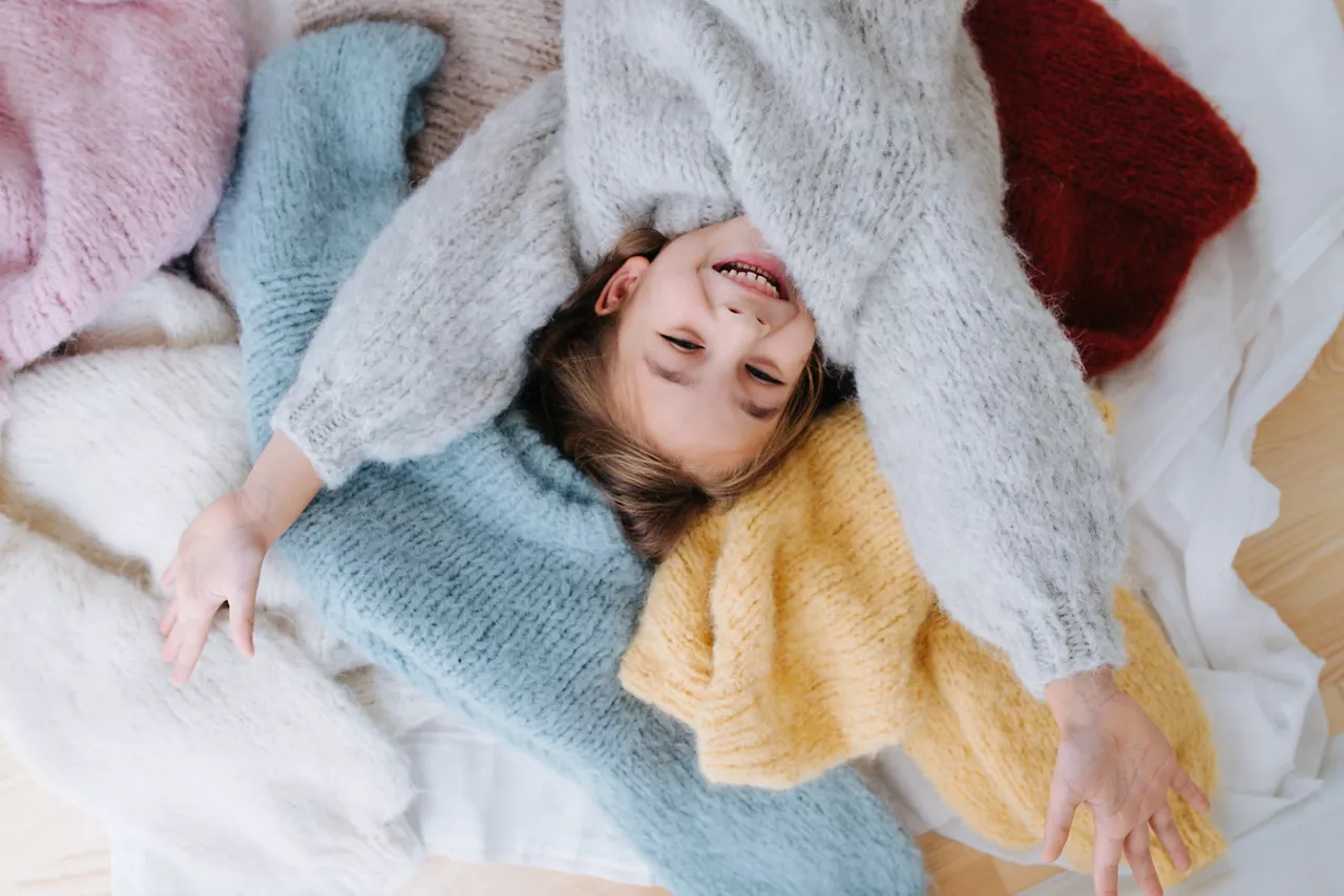Happy child in fluffy sweater, on a pile of colored sweaters