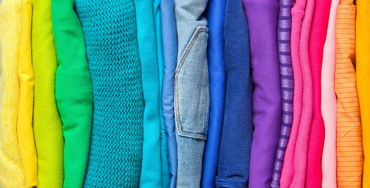 Women's wardrobe sweatshirts shirts and blouses hang on wooden shoulders in the order of all the colors of the rainbow against white brick wall. Concept update in the wardrobe. Advertising space  