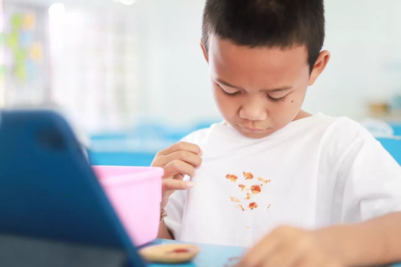 Asian kid showing dirty sauce or food stain on shirt from eating in meal. dirty stain for cleaning concept.