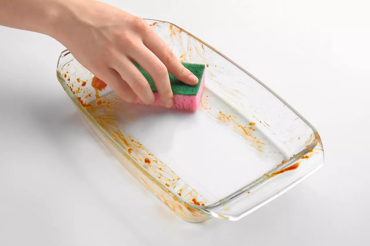 Woman cleaning baking dish on white background