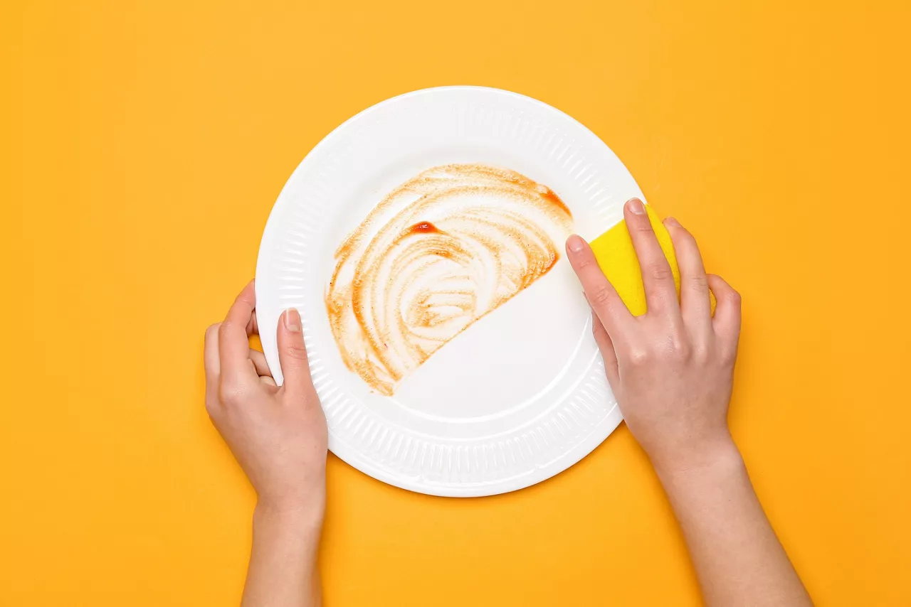 Woman washing dirty plate on orange background