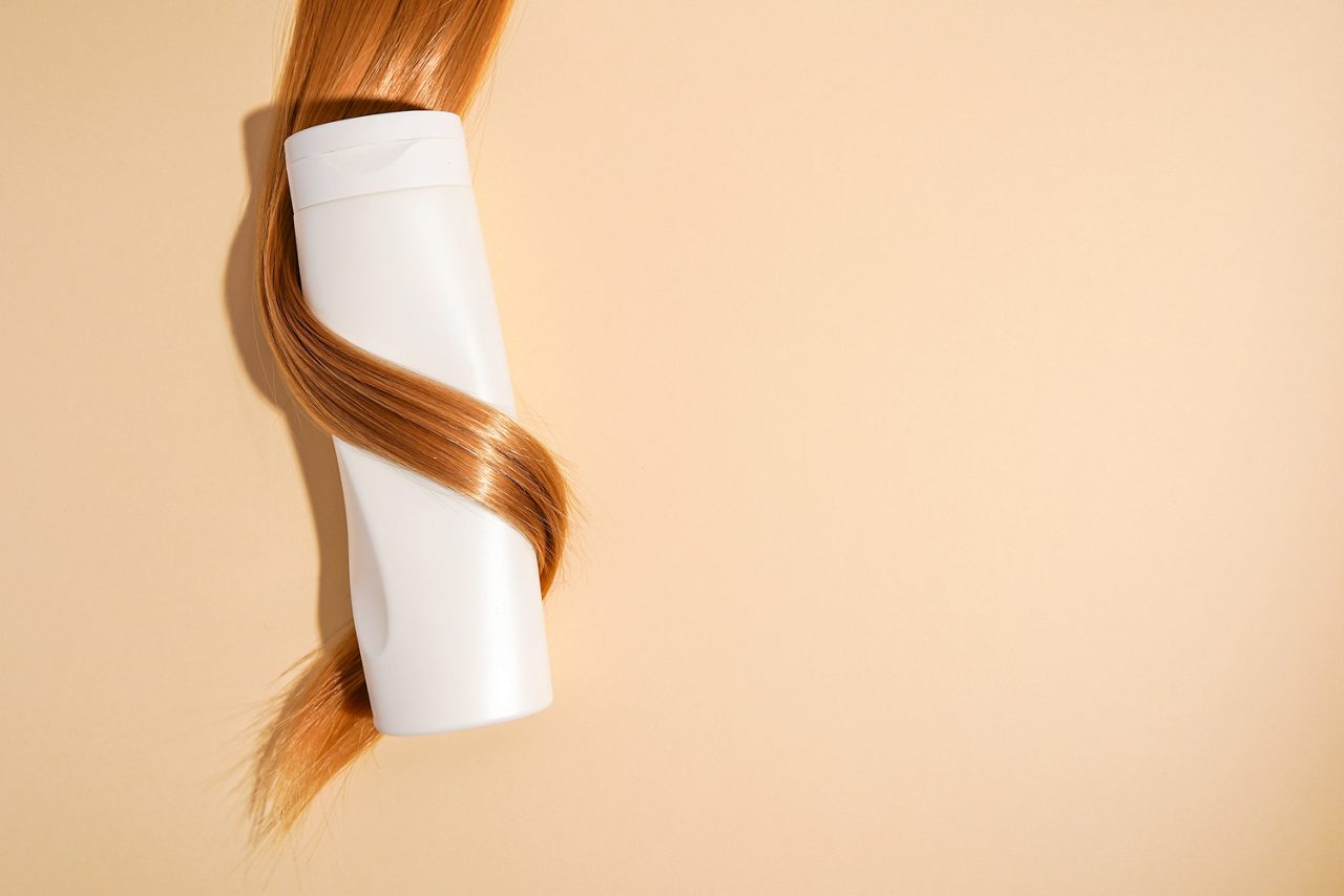 Blond hair curled around shampoo bottle close-up on light background, copy space