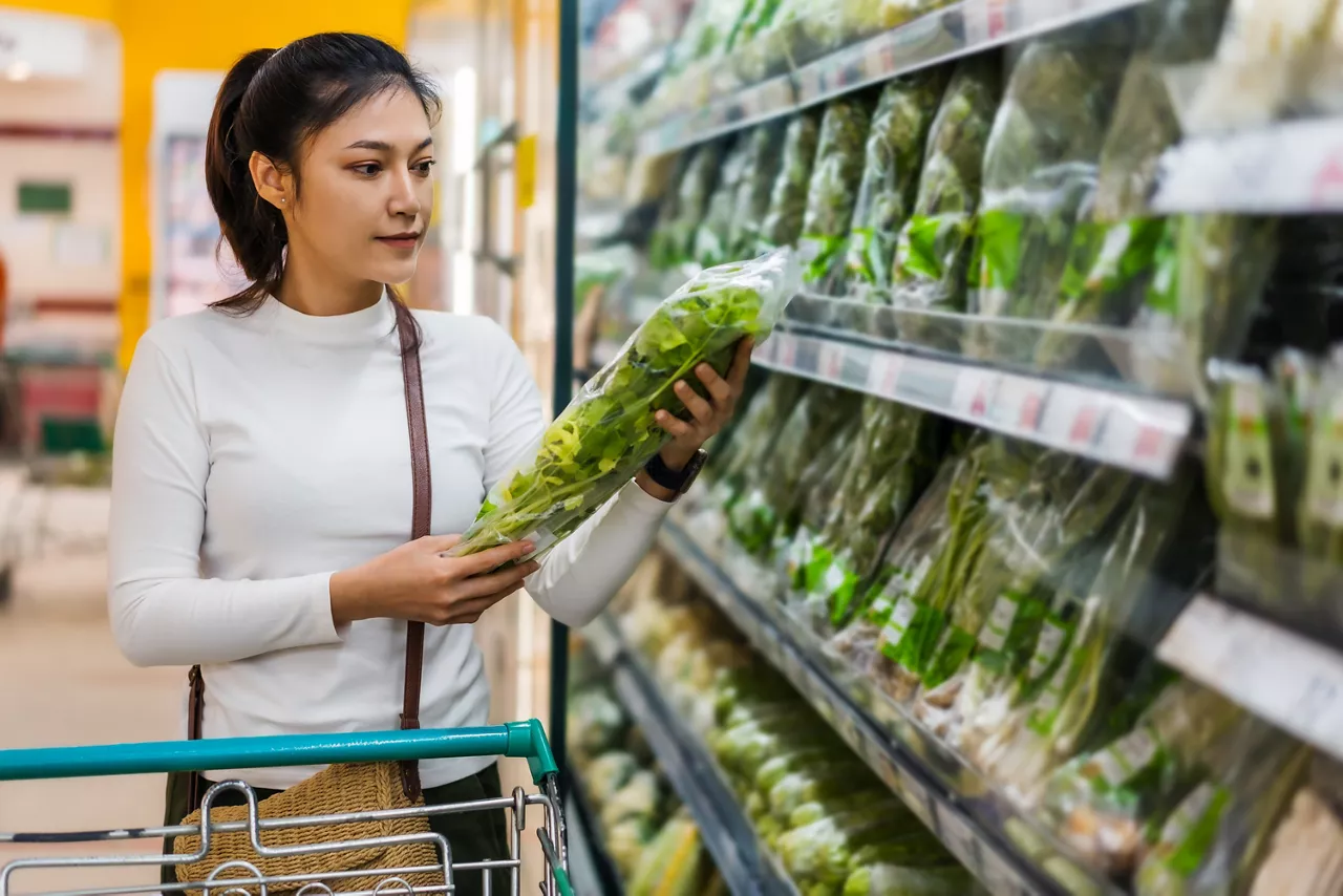 young Asian woman choosing vegetables while shopping food in supermarket