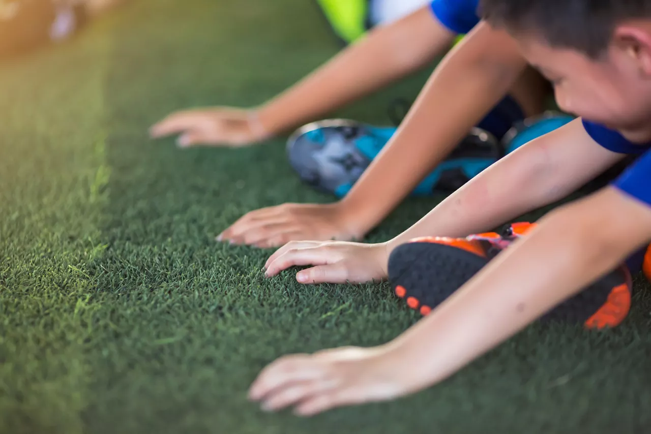 Children's hands on green artificial turf. Hand sensitivity test competition. Kid soccer are training in the football academy.