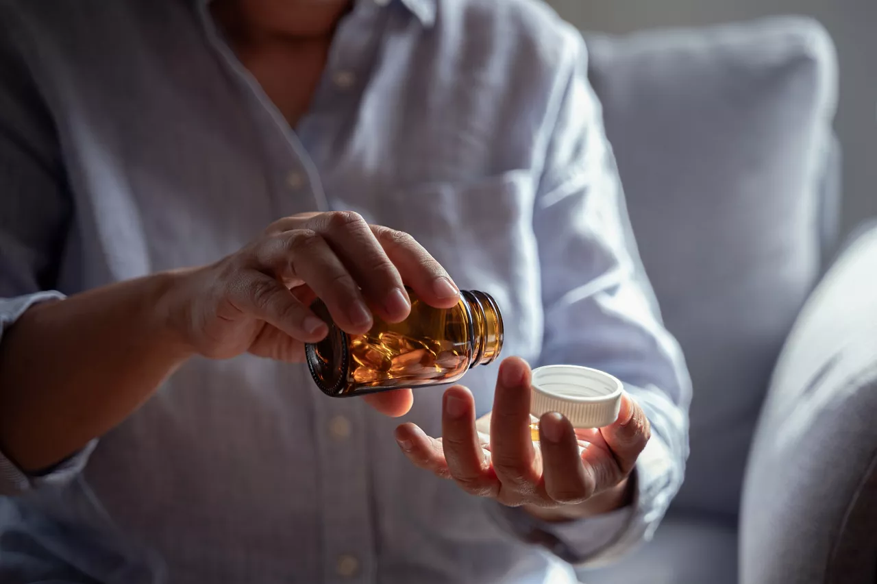 Close up hand of an elderly Asian woman is pouring vitamins from a bottle to take for boosting her immune system and nourishing her body. Senior people health care vitamin product concept.
