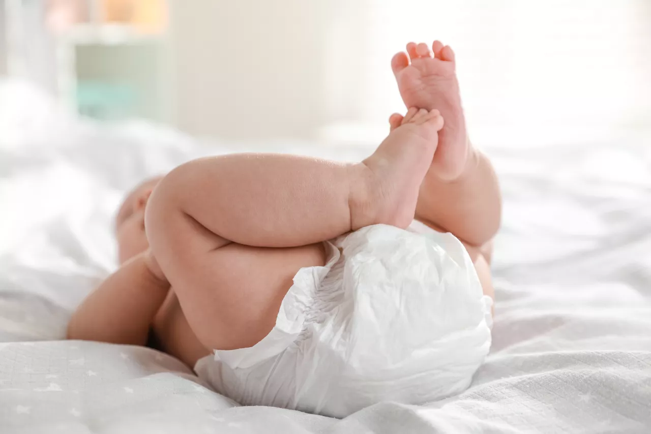 Cute little baby in diaper on bed indoors, closeup