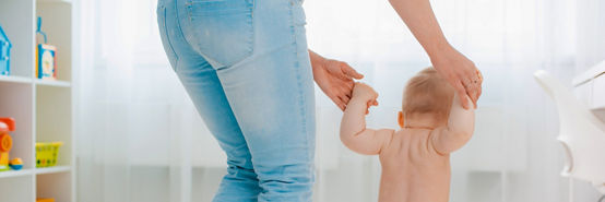 Cute little baby in a diaper learning to walk in a white room , mom holding his hands